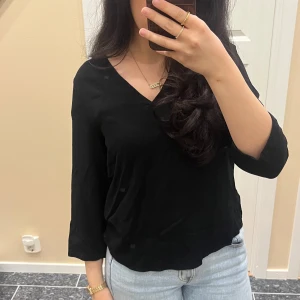 Svart v-ringad blus - Säljer en stilren svart blus med v-ringning och trekvartsärm. Perfekt till jeans eller kjol för en enkel men snygg look. Blusen har en mjuk och lätt känsla.