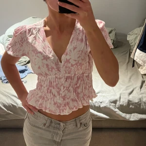 Rosa och vit blommig blus från Primark - Säljer en söt blus från Primark i rosa och vitt blommigt mönster. Blusen har korta puffärmar, v-ringning och volangdetalj nedtill. Perfekt för vår och sommar! Pris kan diskuteras!!