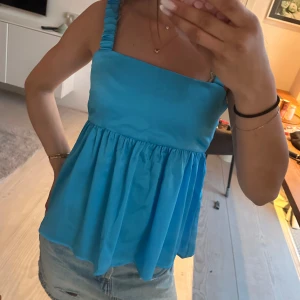 Blå linnetopp med knytband - Säljer en blå linnetopp med breda axelband och knytning i ryggen. Toppen har en luftig och lätt utsvängd passform, perfekt för varma dagar. Snygg att matcha med jeans eller shorts!Hlet ny med prislapp kvar!Nypris 700, mitt pris 200