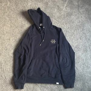 Mörkblå hoodie från Les Deux - Säljer en mörkblå hoodie från Les Deux med broderad logga på bröstet. Tröjan har huva med dragsko och en stor magficka framtill. 