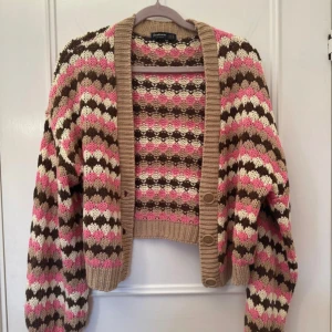 Mönstrad kofta från Stradivarius - Säljer en stickad kofta från Stradivarius i storlek S. Koftan har ett mönster i rosa, beige, brunt och vitt, med ribbade muddar och tre knappar framtill. Perfekt för lager-på-lager och ger en retrovibe till din outfit❤️❤️Aldrig använd, fått som present❤️