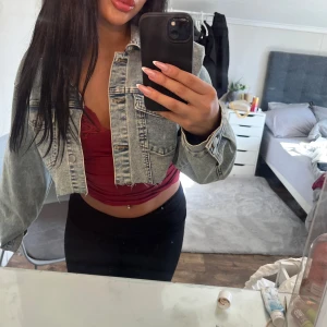 Croppad jeansjacka i ljus denim - Säljer en croppad jeansjacka i ljusblå denim med klassiska bröstfickor och knappar framtill. Jackan har lång ärm och rå kant nertill för en trendig look. Perfekt för dig som vill ha en cool och avslappnad stil.