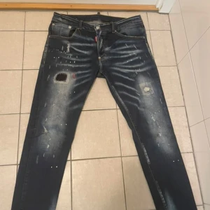 Exklusiva Dsquared2 “ICON” Jeans – Trendiga & Unika! - Säljer ett par snygga och äkta Dsquared2 jeans med ikonisk “ICON”-patch på baksidan. Jeansens slitningar, färgstänk och design ger en modern och stilren look – perfekt för dig som vill sticka ut med klass! Väldigt sparsamt använda och i fint skick. Nypris över 4000 kr