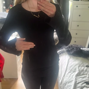 Svart ribbad långärmad topp - Säljer en svart långärmad topp med ribbad struktur och lätt volang vid ärmslut. Sitter tight och är stretchig, perfekt till många olika outfits. Enkel och stilren design utan synliga loggor.
