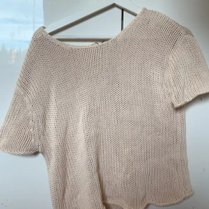 Beige stickad kortärmad tröja - Säljer en beige stickad tröja med korta ärmar och rund hals. Tröjan har en avslappnad passform och är perfekt för lager-på-lager-stil. Enkel och stilren design som passar till mycket.