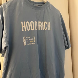 Ljusblå t-shirt från Hoodrich - Ljusblå t-shirt från Hoodrich med vit text och tryck både fram och bak. Oversized passform och rund halsringning. Perfekt för en avslappnad streetwear-look.