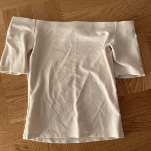 Vit offshoulder topp - Säljer en stilren vit offshoulder topp med korta ärmar. Toppen har en rak halsringning och är tillverkad i ett mjukt bomullsmaterial. Perfekt för dig som gillar en enkel och trendig look.