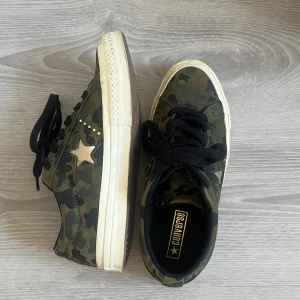 Converse  - Säljer ett par Converse sneakers i grönt camouflage-mönster med svarta skosnören och vit sula. Skorna har en stjärndetalj på sidan och klassisk Converse-logga på plösen. Använda få gånger och köptes för 1200 ca 1 år sen🙃