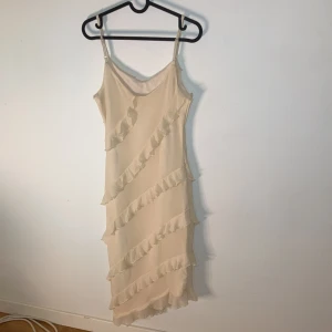 Beige volangklänning från SHEIN - Supersöt beige klänning från SHEIN med smala axelband och volangdetaljer som går diagonalt över hela klänningen. Lätt och flowy känsla, perfekt för varma dagar eller speciella tillfällen.