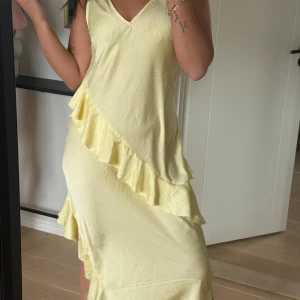 Ljusgul klänning med volang - Säljer en ljusgul klänning med v-ringning och volangdetalj som går diagonalt över framsidan. Klänningen har ärmlös design och är tillverkad i ett lätt material, perfekt för varma dagar💛💛