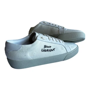 Vita Saint Laurent sneakers i canvas - Snygga vita sneakers från Saint Laurent med handskriven logga på sidan. Skorna har ovandel i canvas och detaljer i skinn, klassisk snörning och platt sula. Perfekta för en clean och stilren look. Kommer med originalkartong.