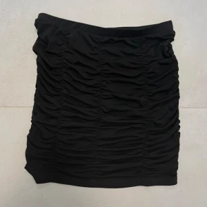 Svart kortkjol från Noisy May - Säljer en svart kortkjol från Noisy May med snygga rynkade detaljer som ger en cool och trendig look. Kjolen är figurnära och stretchig. Passar S/M