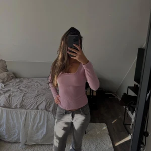 Ljusrosa ribbad långärmad topp - Supersöt ljusrosa ribbad topp med lång ärm och fyrkantig ringning. Små spetsdetaljer längs urringningen ger en extra gullig touch. Sitter figurnära och är perfekt att styla med jeans eller kjol.