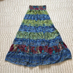 Färgglad långkjol från Boho Fashion - Maxikjol med bohemiskt paisleymönster i blått, grönt, rött och turkost. Kjolen har bred resår i midjan och är sydd i flera volanger för extra flow. Perfekt för dig som gillar färg och mönster! Passar S/M, endast använd ett par fåtal gånger 