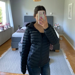 Svart dunjacka Peak Performance 160 - Lättviktig dunjacka från Peak Performance — Frost-modellen med huva. Perfekt till höst/vår eller som isolerande lager vintertid. Jackan är välvårdad och ser nästan ut som ny. Nypris ligger normalt runt 2000kr, köptes på rea för ca 1500 kr. Jag säljer den nu för 800 kr — ett riktigt kap för en kvalitetsjacka i mycket fint skick!