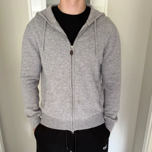Grå kashmir hoodie från Sayless - Mjuk och lyxig grå hoodie från Sayless i kashmir. Tröjan har dragkedja framtill, huva med snörning och ribbade muddar. Perfekt för dig som vill ha en stilren och bekväm look med premiumkänsla. Storlek M passar någon som är 175-185. Mycket bra skick, mitt pris 649:- nypris 999:-