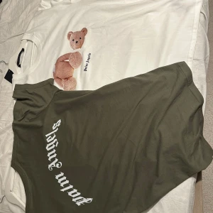 Palm Angels t-shirt med björn - Säljer två Palm Angels t-shirts. Ena är vit med ett broderat nallemotiv och Palm Angels-tryck, andra är olivgrön med stort Palm Angels-tryck i vitt på ryggen. Båda har rund hals och är kortärmade, tillverkade i mjuk bomull. Perfekt för dig som gillar streetwear och snygga prints. 700 för båda