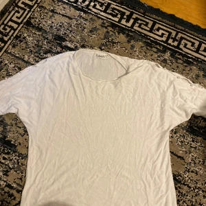 Vit t-shirt med pärlknappar från Dear - Vit t-shirt från Dear med rund halsringning och snygga pärlknappar på axlarna som extra detalj. T-shirten är i mjukt material och har en avslappnad passform. Perfekt för dig som gillar stilrena plagg med en twist.