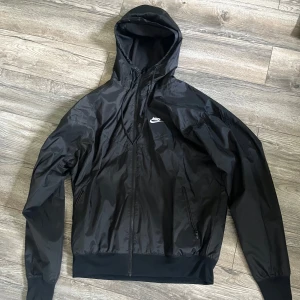 Svart Nike vindjacka  - Svart vindjacka från Nike med huva och dragkedja framtill. Inte alls använd, väldigt bra materiel och därför också i bra skick. Pris kan diskuteras.