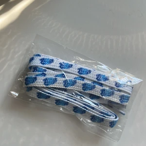 Billys, skosnören - Fräscha vita skosnören med blå Billys-logga tryckt längs hela snöret. Perfekt för att ge dina sneakers en unik och personlig touch. Passar de flesta sneakers och är enkla att trä på.