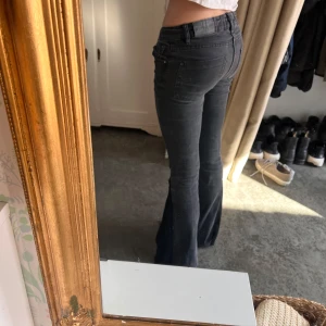 Svarta bootcut jeans med låg midja - Säljer ett par svarta jeans med bootcut-modell och låg midja. Jeansen har klassisk femficksdesign och är i ett stretchigt denimtyg som sitter snyggt över höfterna och låren innan de släpper ut vid vaden. Perfekta för dig som gillar en retro vibe. Omsydda till bootcut