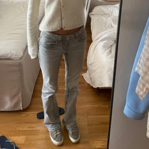 Ljusgrå bootcut jeans låg midja - Säljer ett par ljusgrå jeans med låg midja och bootcut. Jeansen har klassiska fem fickor, snygga sömmar och är tillverkade i mjukt denimtyg. Perfekta för dig som gillar en avslappnad men trendig look.