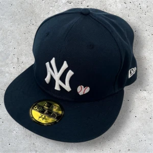 New Era Yankees 59FIFTY keps - Mörkblå 59FIFTY keps från New Era med Yankees-logga framtill, broderad basebollhjärta och texten 'LOVE & HUSTLE = GAME' bak. Snyggt World Series-märke på sidan. Kepsen är i klassisk fitted-modell och tillverkad i 100% polyester.