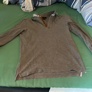 Grå långärmad pikétröja Massimo Dutti - Säljer en grå långärmad pikétröja från Massimo Dutti med casual fit. Tröjan har klassisk krage med öppen hals och diskreta slitsar i sidorna. Perfekt för en chill och stilren look.