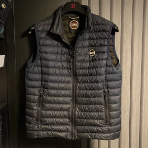 Mörkblå dunväst från Colmar - Snygg mörkblå dunväst från Colmar med dragkedja och två praktiska fickor framtill. Perfekt för lager-på-lager under kyliga dagar. Diskret logotyp på bröstet.