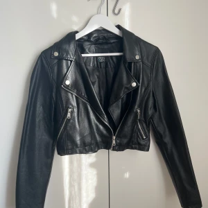 Svart skinnjacka från Even&Odd - Snygg svart skinnjacka från Even&Odd i bikerstil. Jackan är croppad med coola silvriga dragkedjor och detaljer, har långa ärmar och klassisk krage. Perfekt för dig som vill ha en edgy look till din outfit.