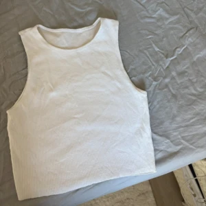 Vit ribbad linnetopp - Enkel och fräsch vit ribbad linnetopp med ärmlös design och rund halsringning. Perfekt att matcha med jeans eller kjol för en clean look. Mjuk och skön mot huden, passar till varma dagar.