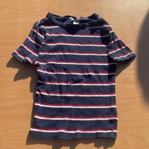 Randig t-shirt från H&M Divided XS - Mörkblå ribbad t-shirt från H&M Divided i storlek XS. T-shirten har korta ärmar och är täckt av horisontella ränder i vitt och rött. Materialet är mjuk bomull och passformen är normal. Perfekt för en chill och stilren look.