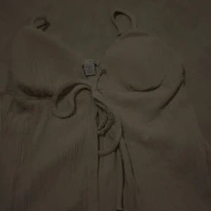 Beige topp från AMISU (newyorker) - Supersöt beige topp från AMISU (newyorker) med smala axelband och knyt i midjan. Toppen har en lätt struktur i tyget och en feminin passform med markerad byst. Perfekt för varma dagar när du vill känna dig extra fin.