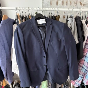 Marinblå kavaj från Zara - Snygg marinblå kavaj från Zara med klassisk passform och två knappar framtill. Kavajen har smala slag, tre fickor och är helfodrad. Perfekt för dig som vill ha en stilren och tidlös look.