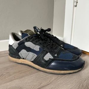 Valentino Rockrunner sneakers, svart/blå - Säljer ett par Valentino Rockrunner sneakers i storlek 44. Ej använda mycket och dom är i bra skick. Perfekt till hösten och vintern. Skorna har en snygg mix av svart, blått och vitt med mesh och mockadetaljer. Sulan har coola nitar och mönster, och skorna har snörning. Perfekt för dig som gillar exklusiva och unika sneakers. 