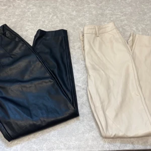 Svarta och beigea byxor i skinnimitation - Två par snygga byxor i skinnimitation, ett par svarta från AMISU i storlek 38 och ett par beigea från FB Sister i storlek S. Båda har klassisk passform med dragkedja och knapp, perfekta för en trendig look.