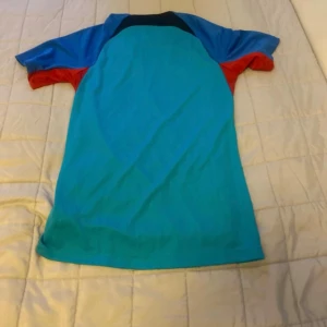 FC Barcelona Nike Dri-Fit fotbollströja XS - Snygg FC Barcelona fotbollströja från Nike i Dri-Fit material. Tröjan är turkos med blå och röda detaljer, svart Nike-logga och FCB-emblem på bröstet. Slim fit-modell med korta ärmar, perfekt för träning eller match.