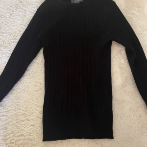 Svart ribbad stickad tröja Primark - Svart långärmad stickad tröja från Primark i storlek S. Tröjan har en ribbad struktur och en klassisk rund halsringning. Perfekt för lager-på-lager och enkel att matcha med olika outfits.