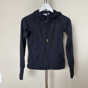 Svart hoodie från Swedemount med dragkedja - Svart träningsjacka från Swedemount med hel dragkedja och huva. Tröjan har långa ärmar och två fickor framtill. Perfekt för chill eller träning, enkel och stilren design med diskret logga på bröstet. Använd mindre än 5 gånger.