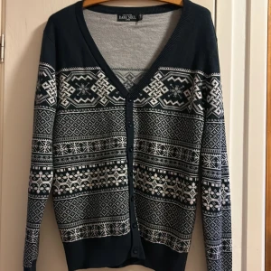 Mörkblå kofta med mönster från Dark Soul - Snygg mörkblå kofta från Dark Soul i storlek L med vitt nordiskt mönster. Koftan har v-ringning, knappar framtill och långa ärmar. Perfekt för kalla dagar och ger en chill vintervibe. Materialet känns mjukt. 