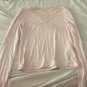 Ljusrosa långärmad topp med spets - Supersöt ljusrosa långärmad topp från Gina Tricot med v-ringning och fina spetsdetaljer runt halsen. Perfekt att styla med jeans eller kjol för en romantisk vibe. Mjuk och skön känsla mot huden. Storlek 146/152 köpt för 199 säljer för 50