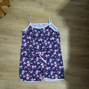 Blommiga shorts med snörning - Söta shorts med blommigt mönster i rosa, lila och vitt på mörkblå botten. De har midja med snörning och vita kanter, samt är gjorda i mjuk bomull. Perfekta för varma sommardagar och chill hemma.