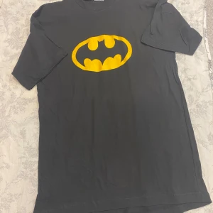 Svart Batman t-shirt med gul logga - Svart t-shirt med ikonisk Batman-logga i gult på bröstet. Klassisk passform och rund halsringning, perfekt för dig som gillar superhjältar och vill sticka ut med en cool look. Helt ny , Stlk kvar M, L ,XL 