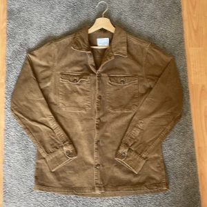 Brun manchester overshirt Jack & Jones - Säljer en brun manchester overshirt från Jack & Jones. Jackan har klassisk krage, två bröstfickor med lock och knappar samt långa ärmar med knapp vid ärmslut. Perfekt för lager-på-lager och chill stil.