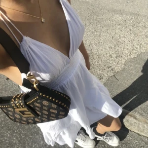 Vit kort sommarklänning med öppen rygg - Superfin vit kort klänning med djup v-ringning och öppen rygg. Klänningen har smala axelband som knyts i nacken och volangkant nertill. Tillverkad i ett lätt, skrynkligt bomullstyg som känns perfekt för varma dagar. I perfekt skick kan fixa fri frakt 