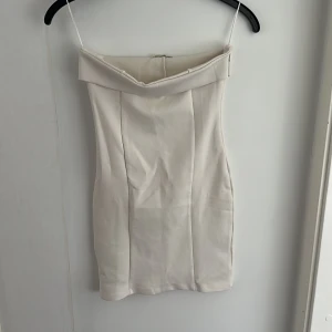Vit axelbandslös kort klänning S - Superfin vit axelbandslös kort klänning med figurnära passform. Helt ny med prislapp kvar. Perfekt för dig som gillar minimalistisk och clean stil. Klänningen har dragkedja på sidan 