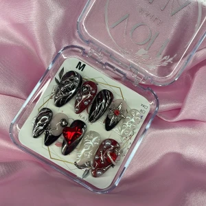 DarkSpell (M);Medium Almond - Snygga gelé lösnaglar i M: 16 mm, 12 mm, 12,5 mm, 11,5 mm, 10 mm  storlek med svart, röd och silver design. Naglarna har 3D-dekorationer som pärlor, hjärtan och stjärnor samt metallicdetaljer. Mix av glittriga och chrome/cateye ytor, vissa med swirlmönster och andra med pärlrelief. Perfekt för dig som vill sticka ut.