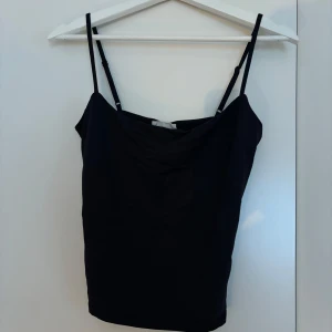 Svart linnetopp från Gina Tricot - En stilren svart linnetopp från Gina Tricot, basically basics-kollektionen. Toppen har tunna justerbara axelband och en enkel, rak passform. Perfekt att matcha med jeans eller kjol för en clean look.