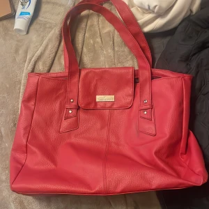 Röd handväska från Daniel Hechter - Stor och rymlig röd handväska från Don Donna i skinnimitation. Väskan har dubbla axelband, lock med metallbricka och stilren design. Perfekt för dig som vill ha plats för allt du behöver under dagen.