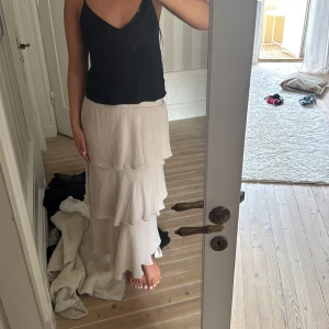 Beige volangkjol med resårmidja - Säljer en lång beige kjol med flera lager volanger och skön resår i midjan. Kjolen har en flowy känsla och är perfekt för dig som gillar en romantisk och avslappnad stil. Passar snyggt till både linne och stickad tröja.